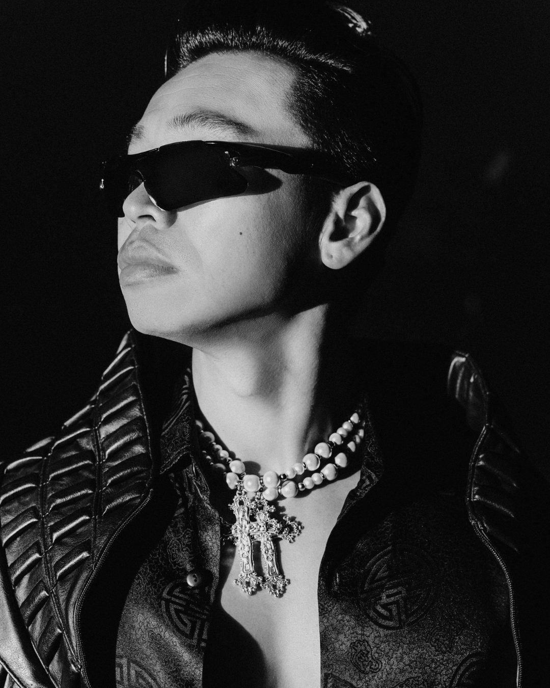 Black-and-white portrait of electronic artist ZHU in wraparound sunglasses, a leather jacket and a pearl-and-cross necklace