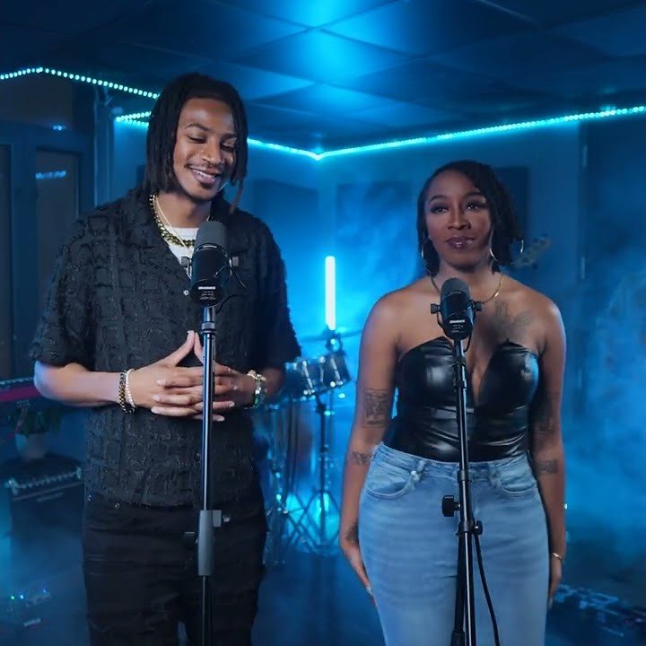 Brandon Bally and vocalist Blair Victoria performing at microphones in a blue-lit studio with a drum kit behind them