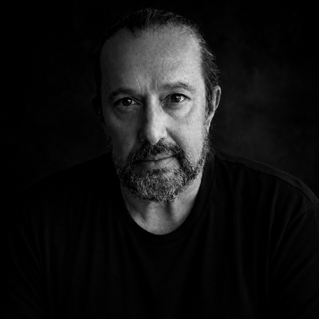 Black-and-white press portrait of Greek composer George Voukanos against a dark background.