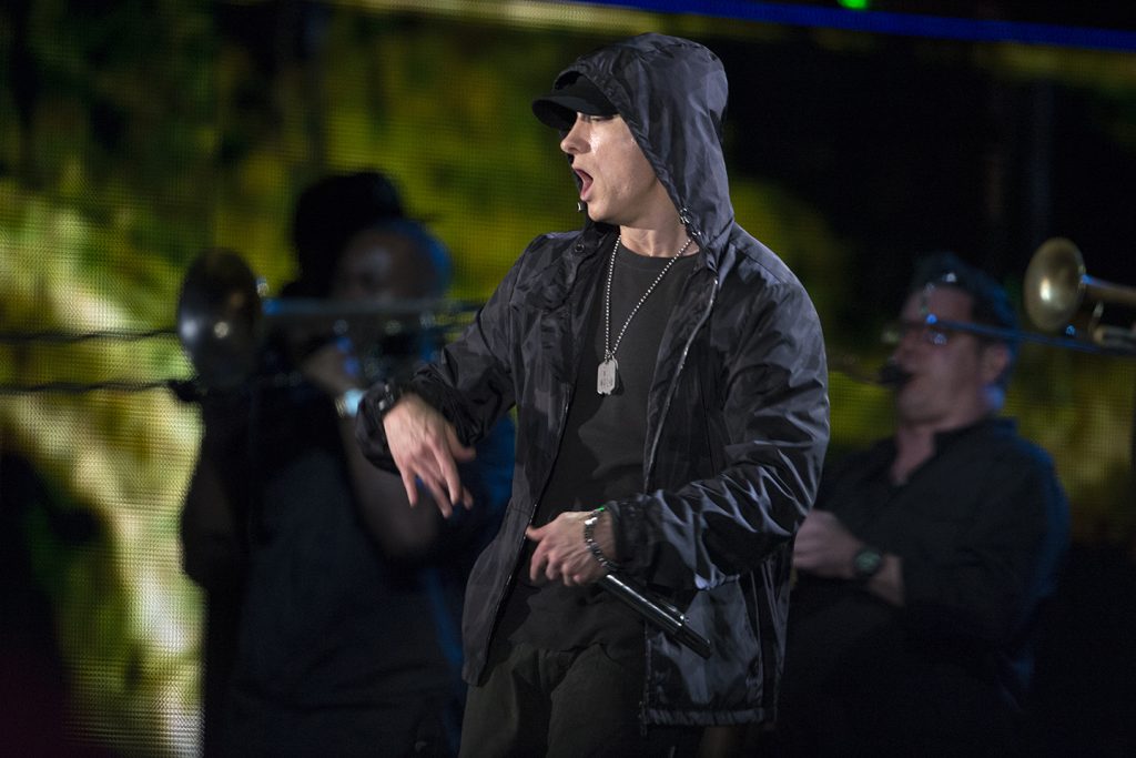 Eminem on stage in a black hooded jacket with the hood up and dog tags around his neck