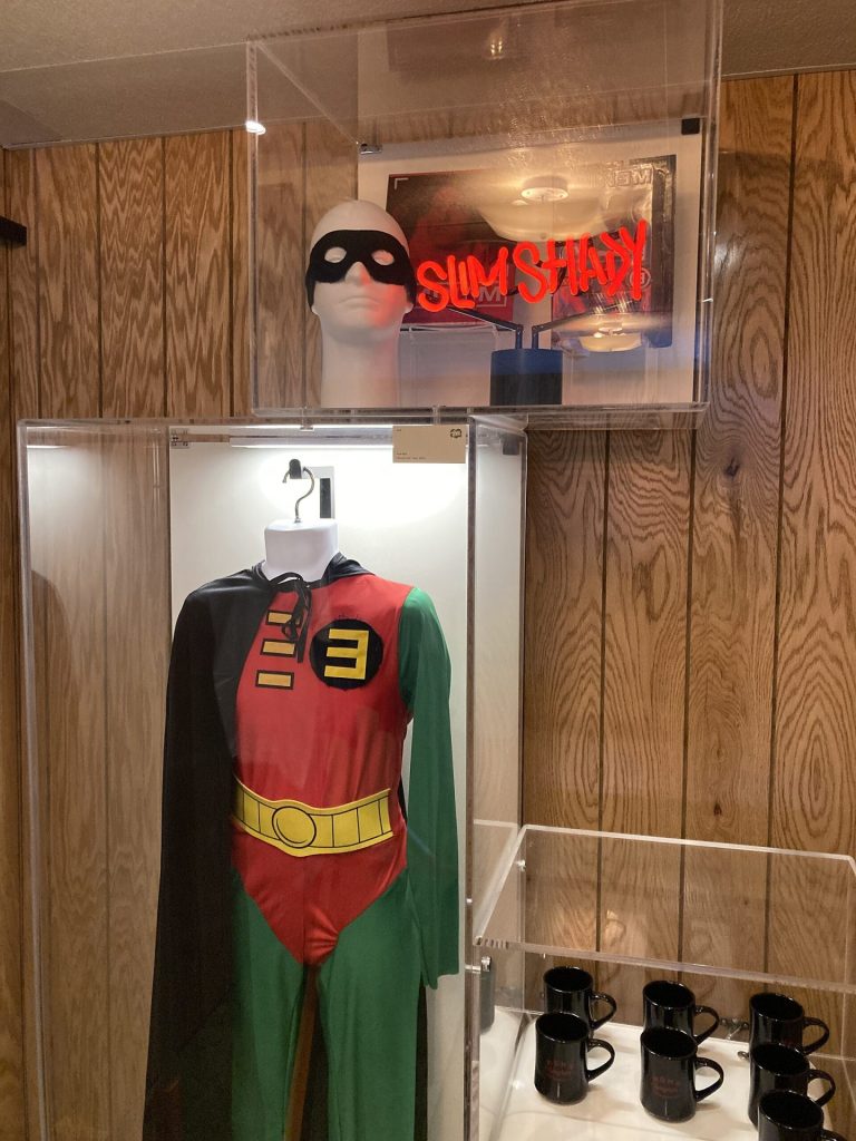 The red, green and yellow Rap Boy superhero costume from the Without Me video displayed in a glass case