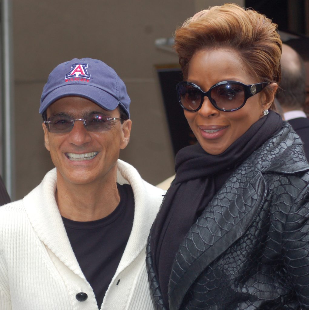Interscope co-founder Jimmy Iovine in a white sweater and ball cap standing next to Mary J. Blige
