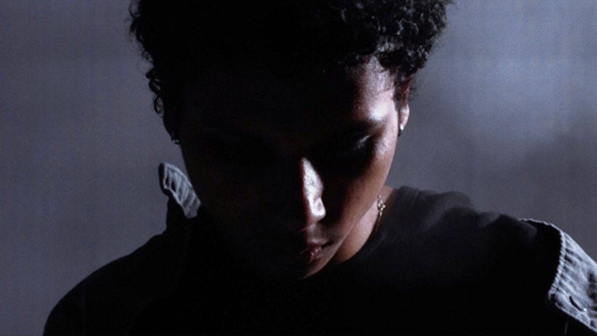 kateo in a still from the "My Love" music video, head bowed under low light