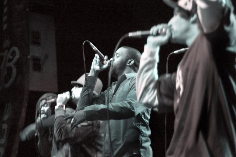 Black-and-white photo of L.A. Symphony members rapping into microphones on a club stage