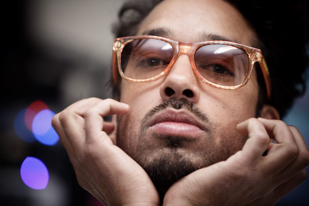 Close-up portrait of Pigeon John in amber sunglasses resting his chin on his hands