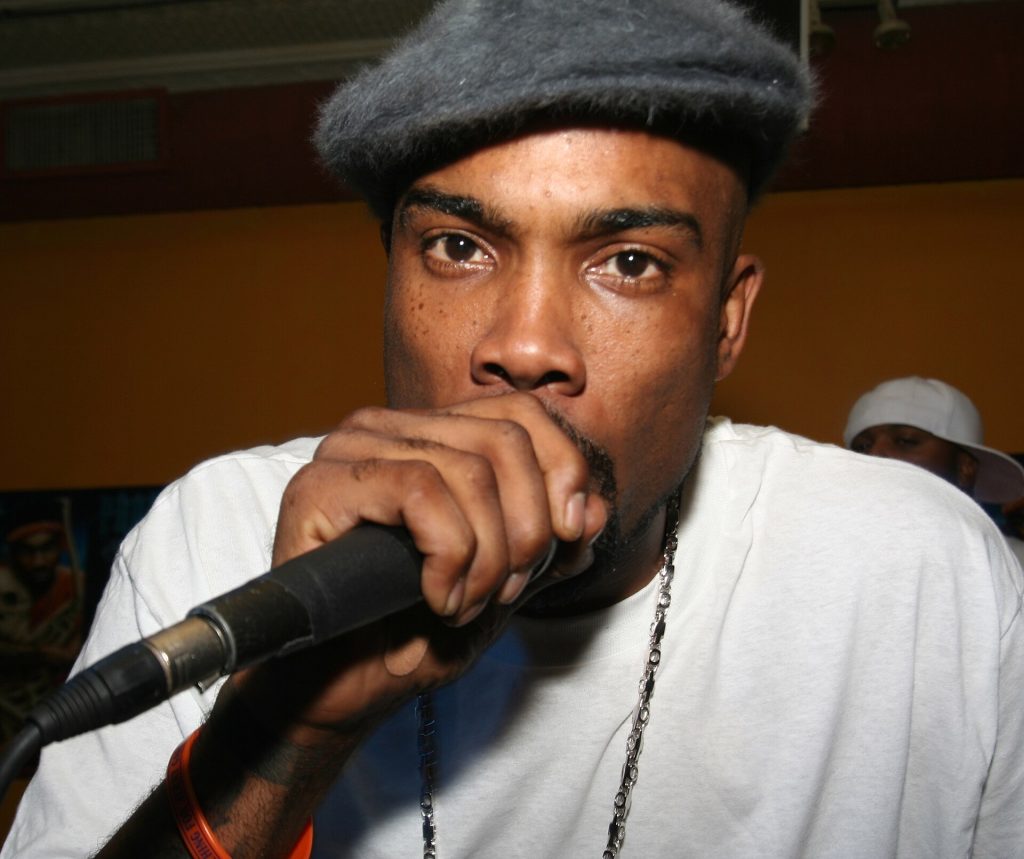 Proof in a gray newsboy cap and white T-shirt rapping into a microphone