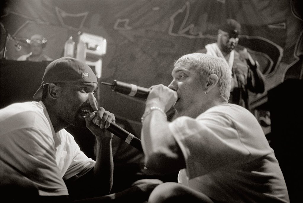 Black-and-white photo of Proof and Eminem rapping face to face on stage, both holding microphones