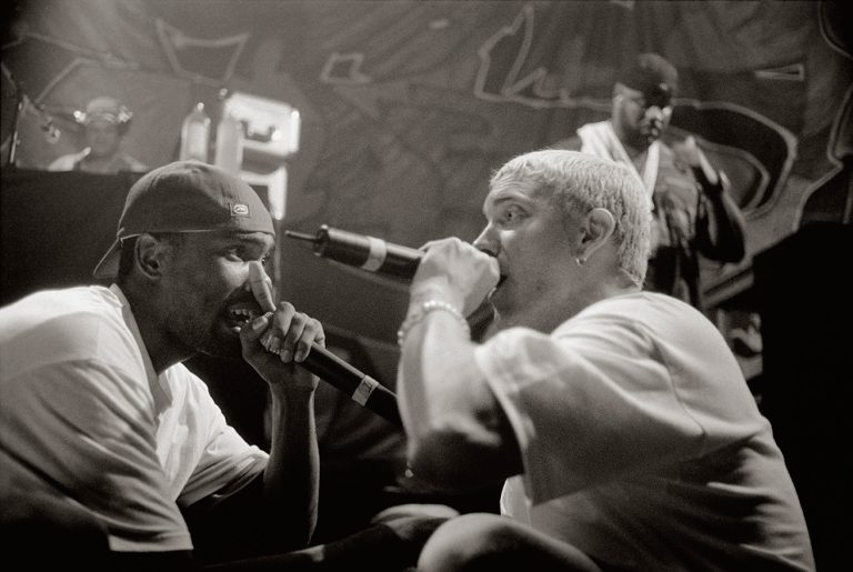 Black-and-white photo of Proof and Eminem rapping face to face on stage, both holding microphones