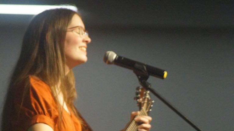 Aby Price singing and playing acoustic guitar at a microphone