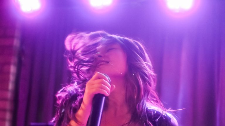 Alyson Indigo singing on stage under purple lights