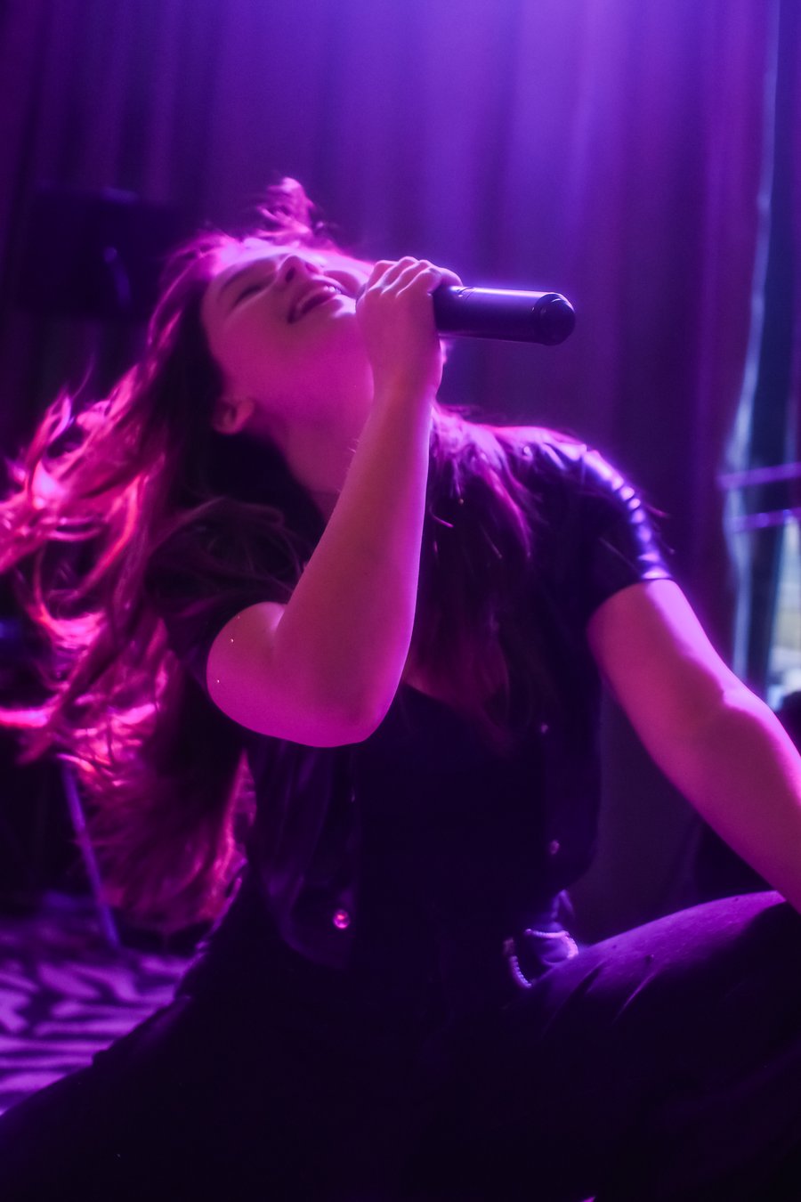 Alyson Indigo singing into a microphone on stage under purple lights