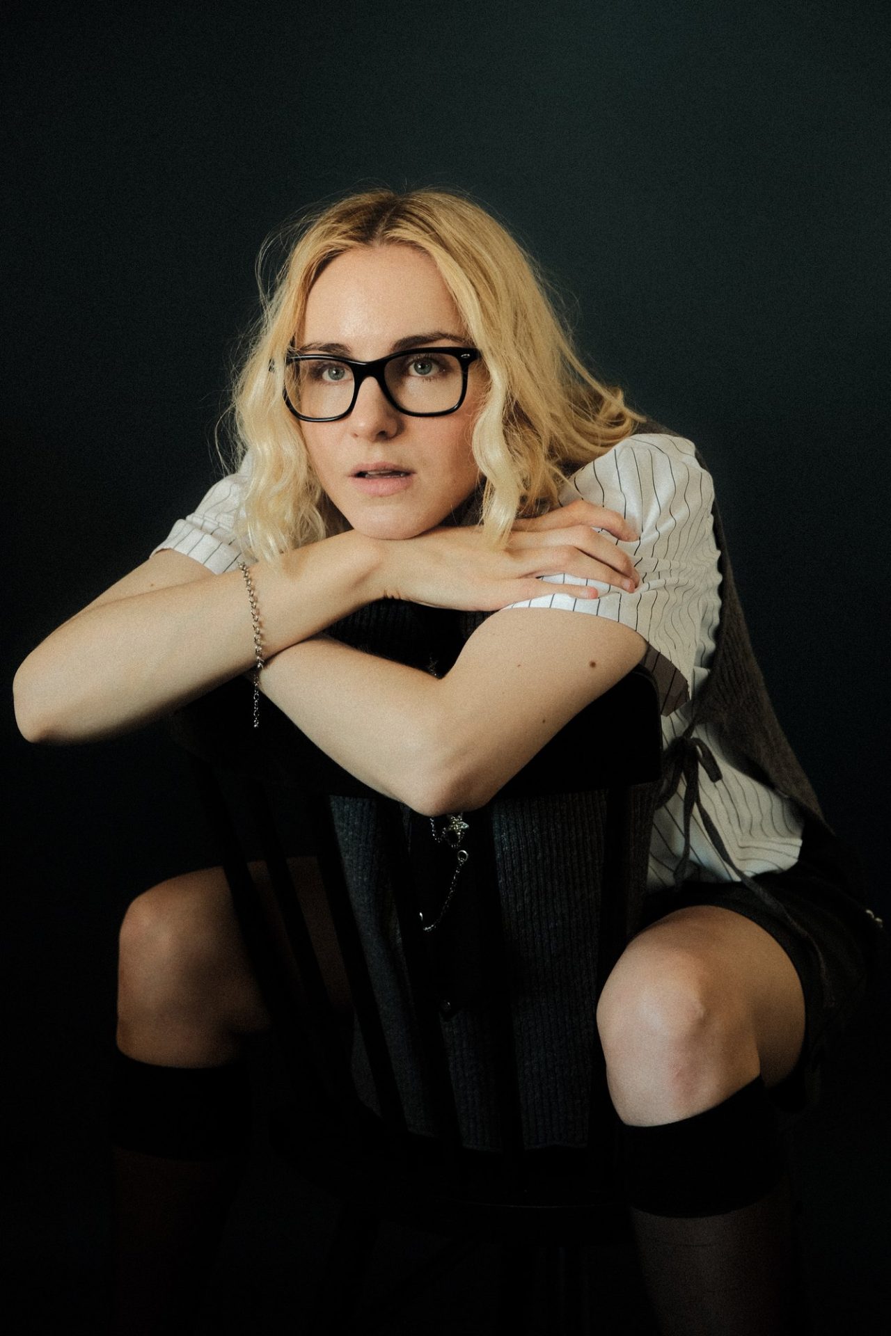 Analesa Fisher, The LA Note digital cover, seated backward on a chair in glasses and a striped shirt
