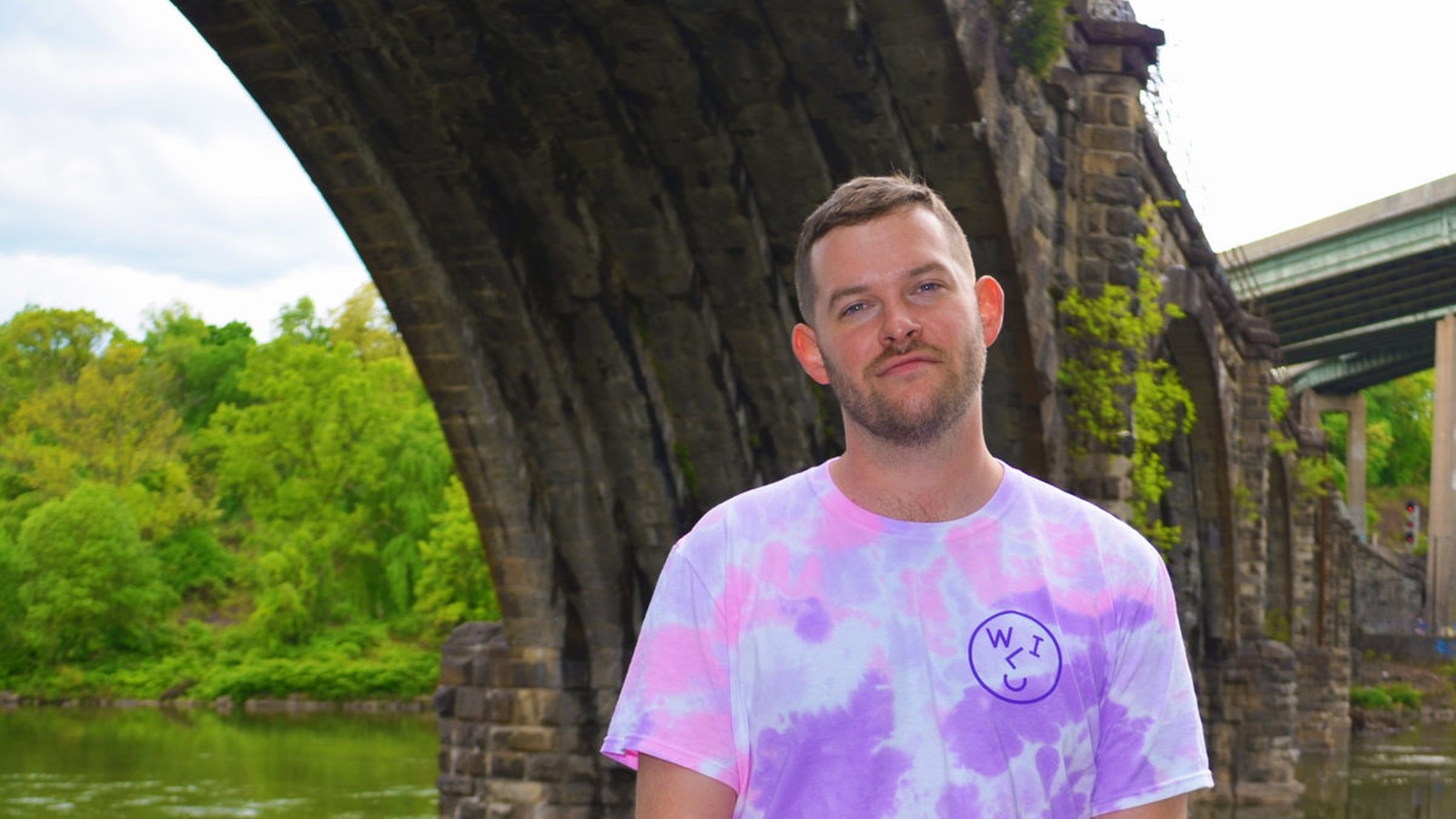 Andrew Huston, Long Beach indie singer-songwriter, seated under a stone bridge