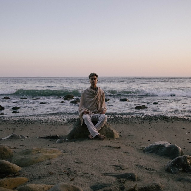 Bryce Lamar seated on a rock on a beach at dusk