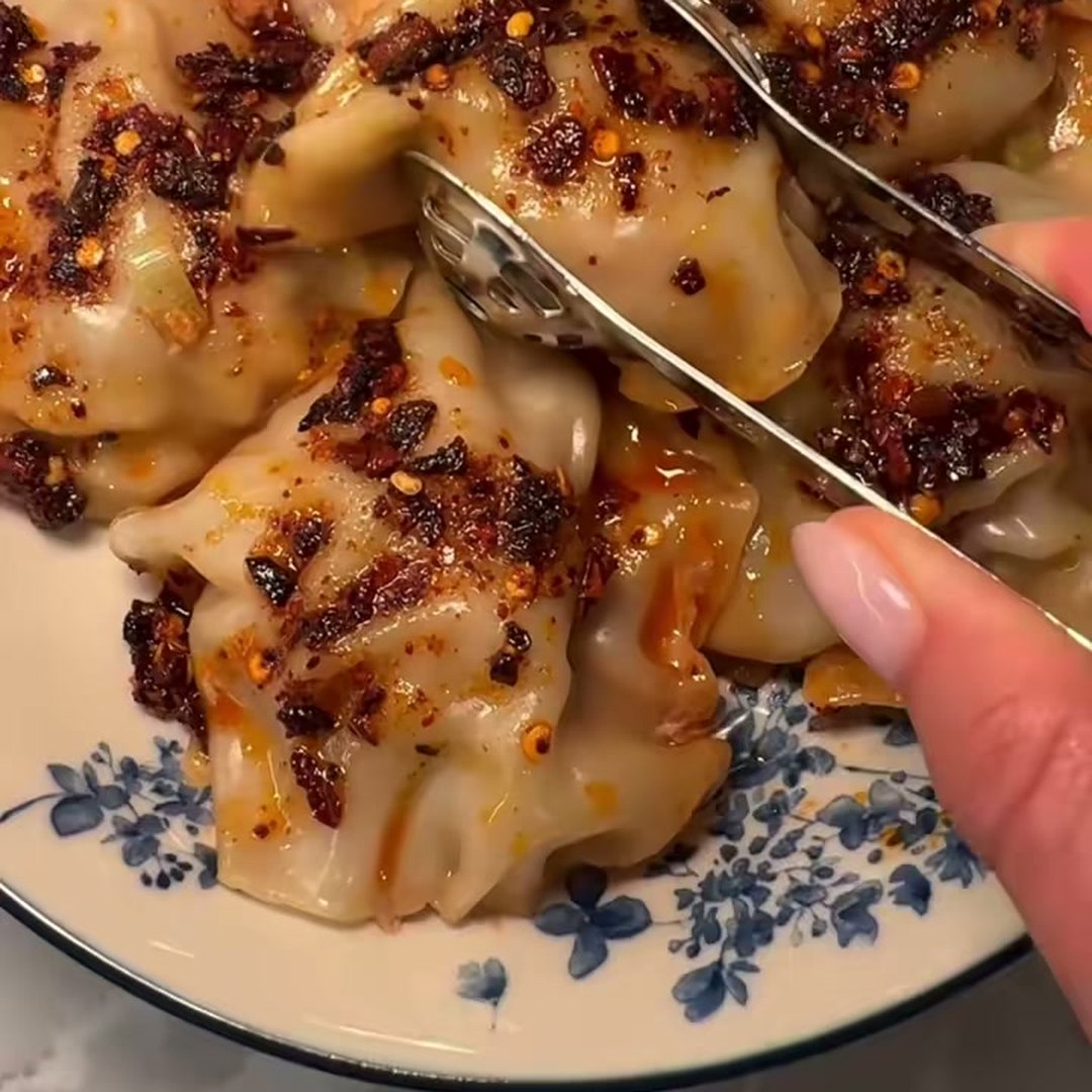 Pan dumplings topped with chili crunch, green onions and sesame seeds in a blue and white bowl