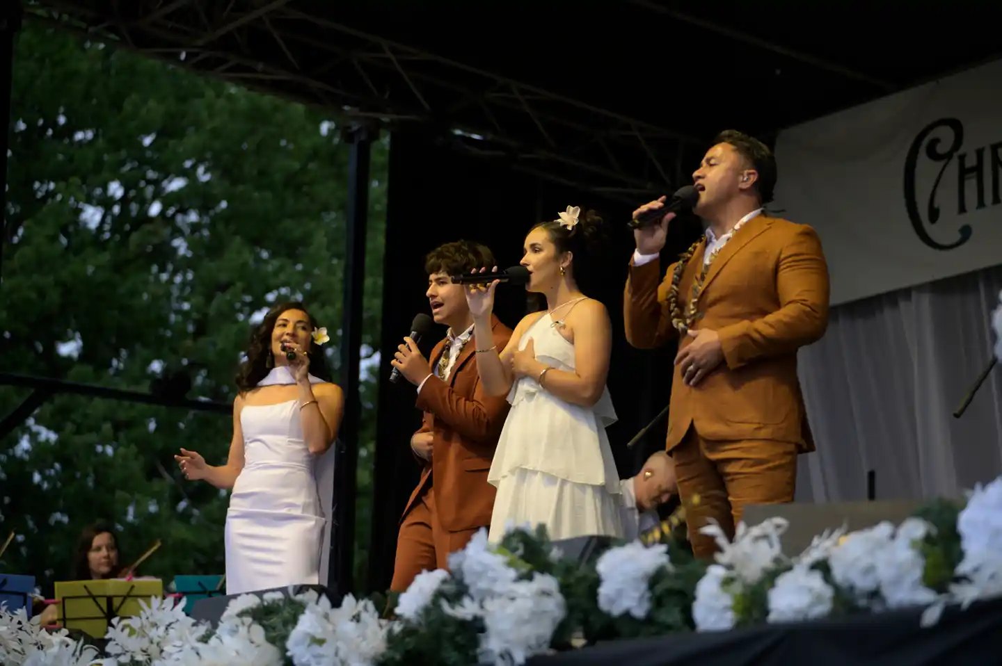 The Amosa Family singing on an outdoor stage decorated with white flowers at their Christmas concert