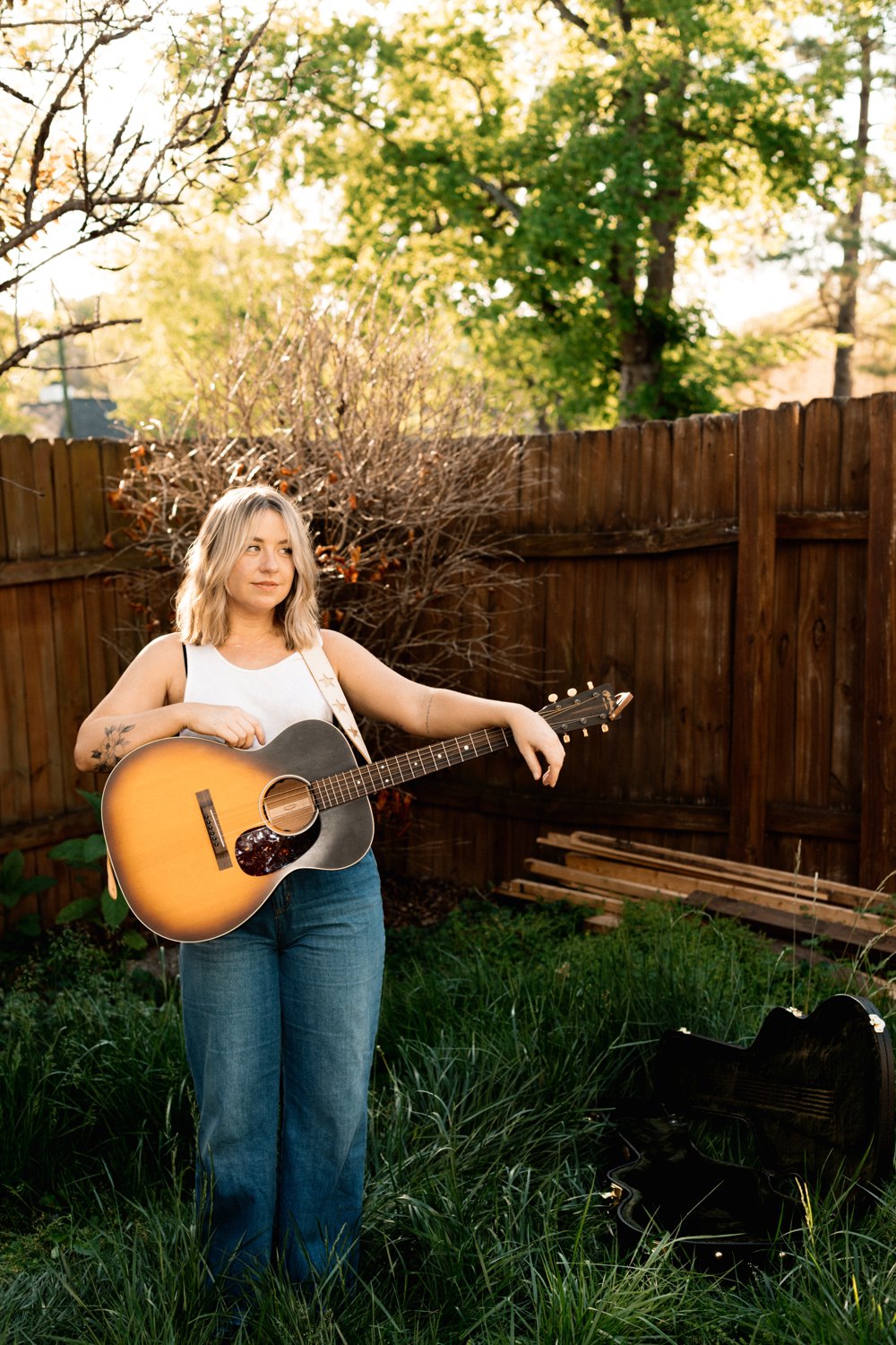 Dani Stacy holding an acoustic guitar in a backyard garden