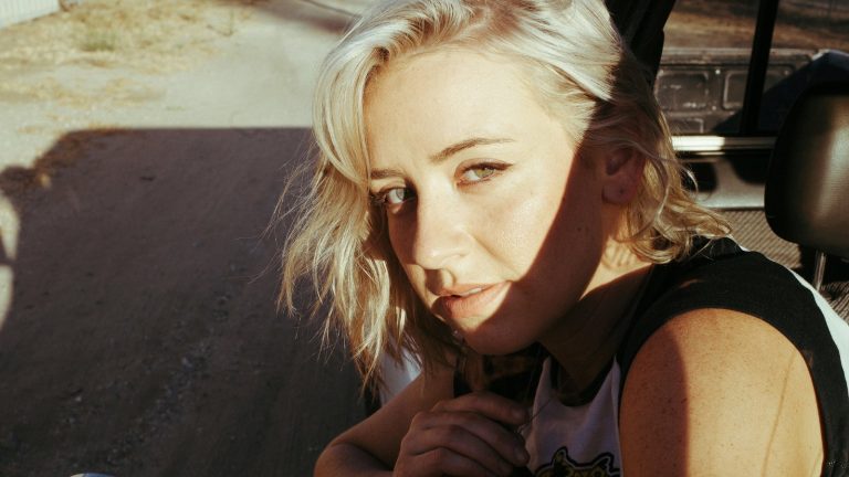 Dani Stacy, blonde singer-songwriter, looking at the camera in warm sunlight