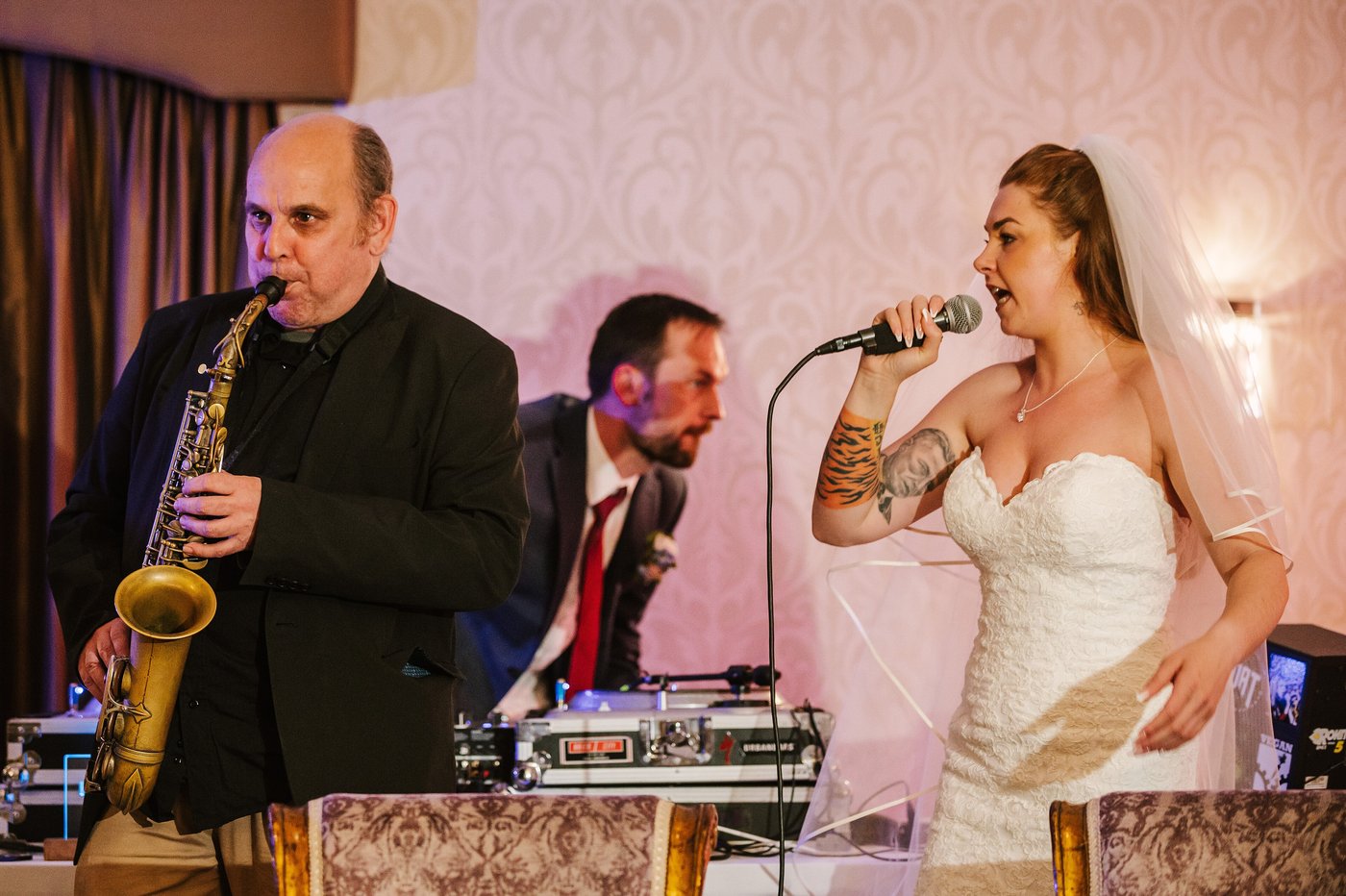 A saxophonist and DJ performing with the bride at a wedding reception