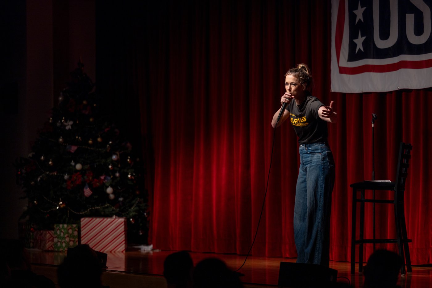 Iliza Shlesinger on a red-curtained stage under a USO banner at Camp Hansen, Okinawa, in December 2024