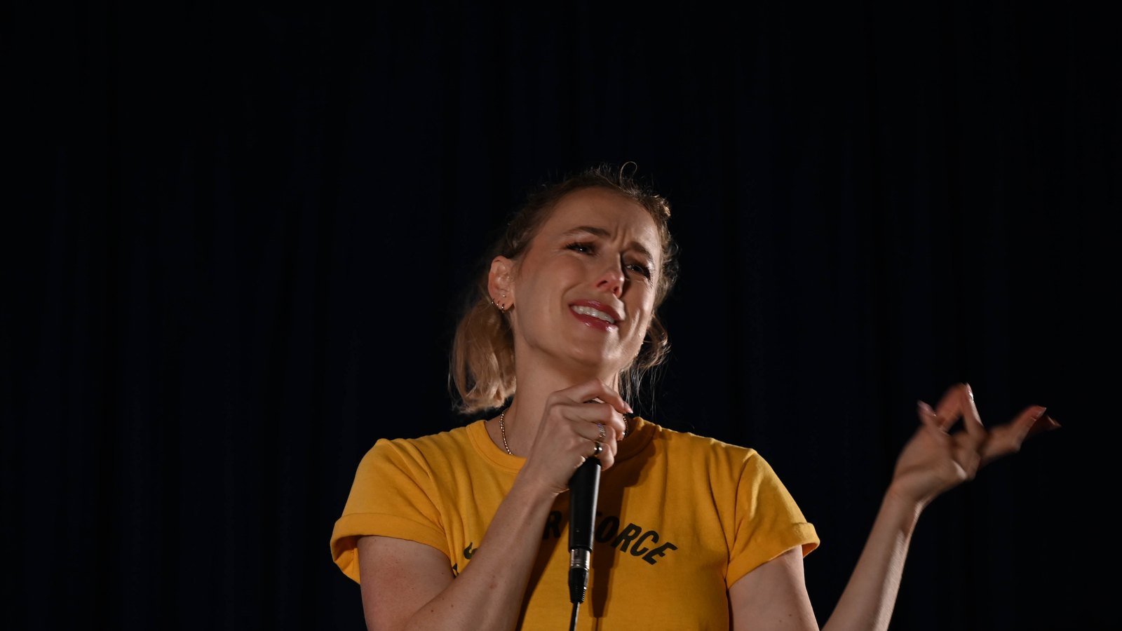 Comedian Iliza Shlesinger performing stand-up in a yellow Air Force T-shirt at Yokota Air Base, Japan, in 2023