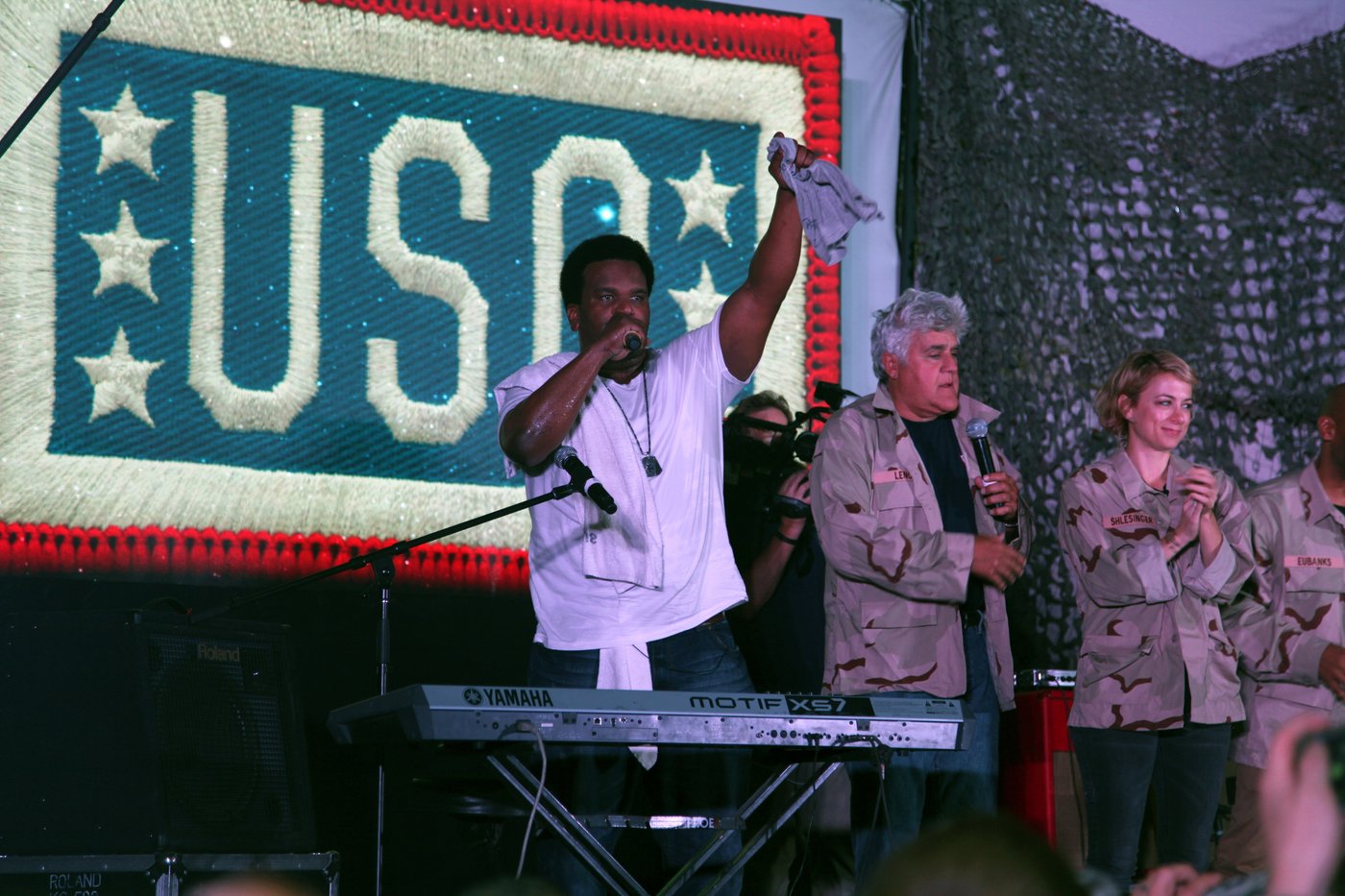 Craig Robinson, Iliza Shlesinger and Jay Leno on stage in front of a USO banner at Bagram Air Field in 2014