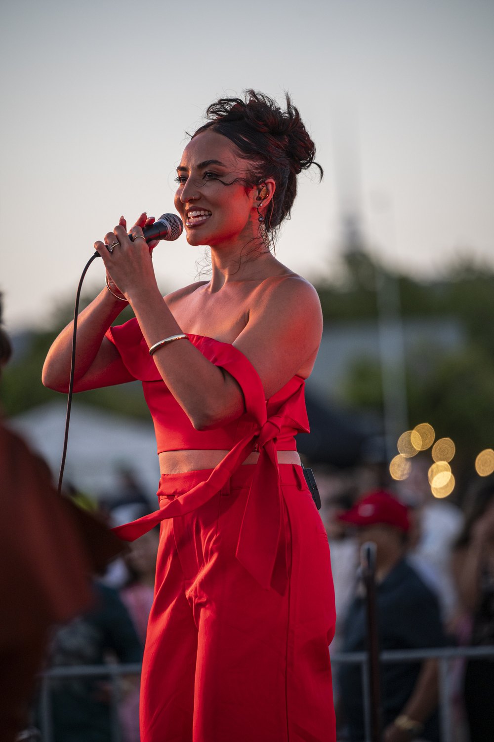 Kirrah Amosa singing into a microphone on an outdoor stage in a red outfit
