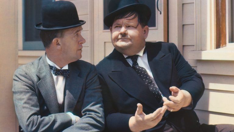 Stan Laurel and Oliver Hardy sitting on a doorstep in their bowler hats, 1938