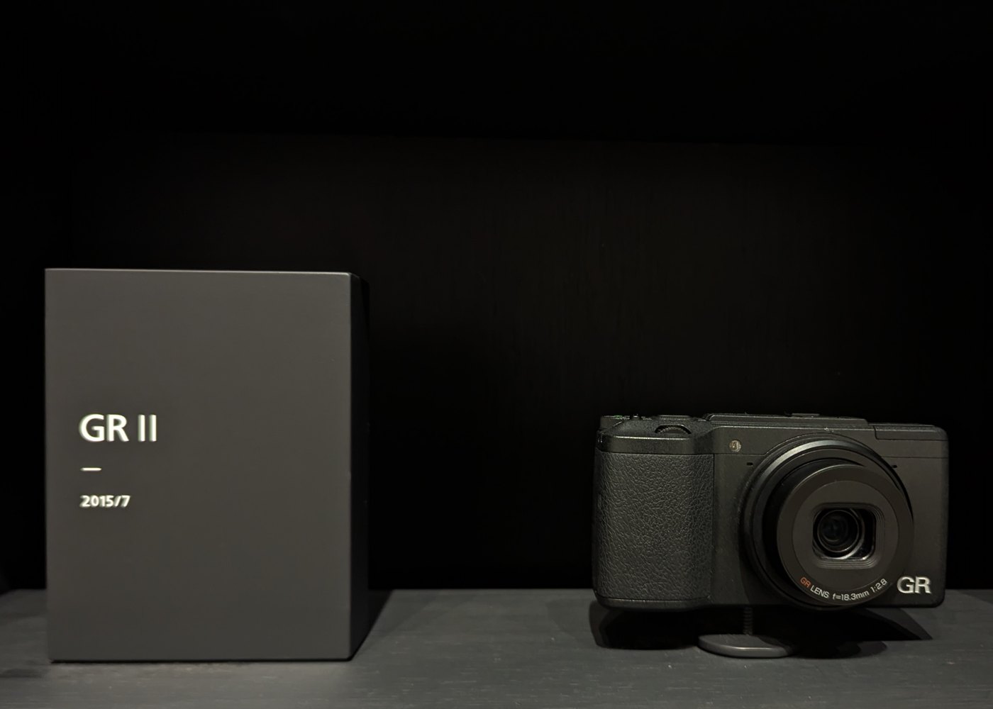 A black Ricoh GR II compact camera on a shelf next to a box labeled GR II