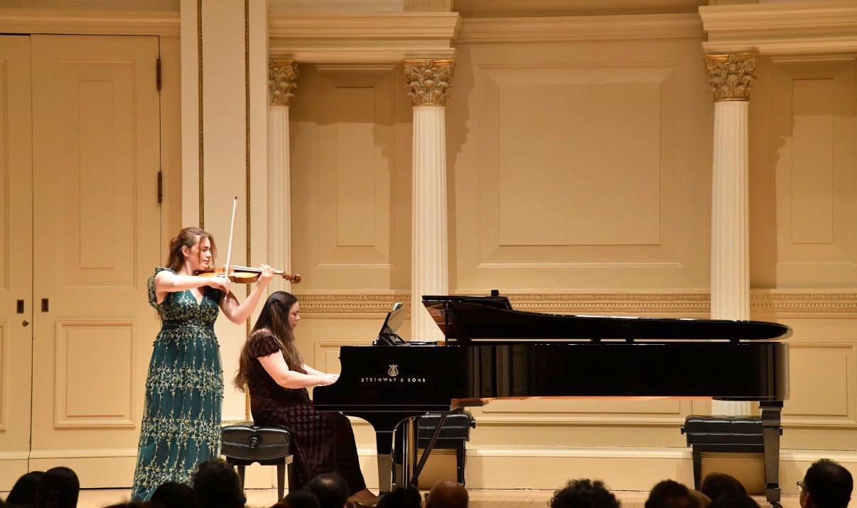 Sendi Vartanovi performing violin with a pianist on a concert stage