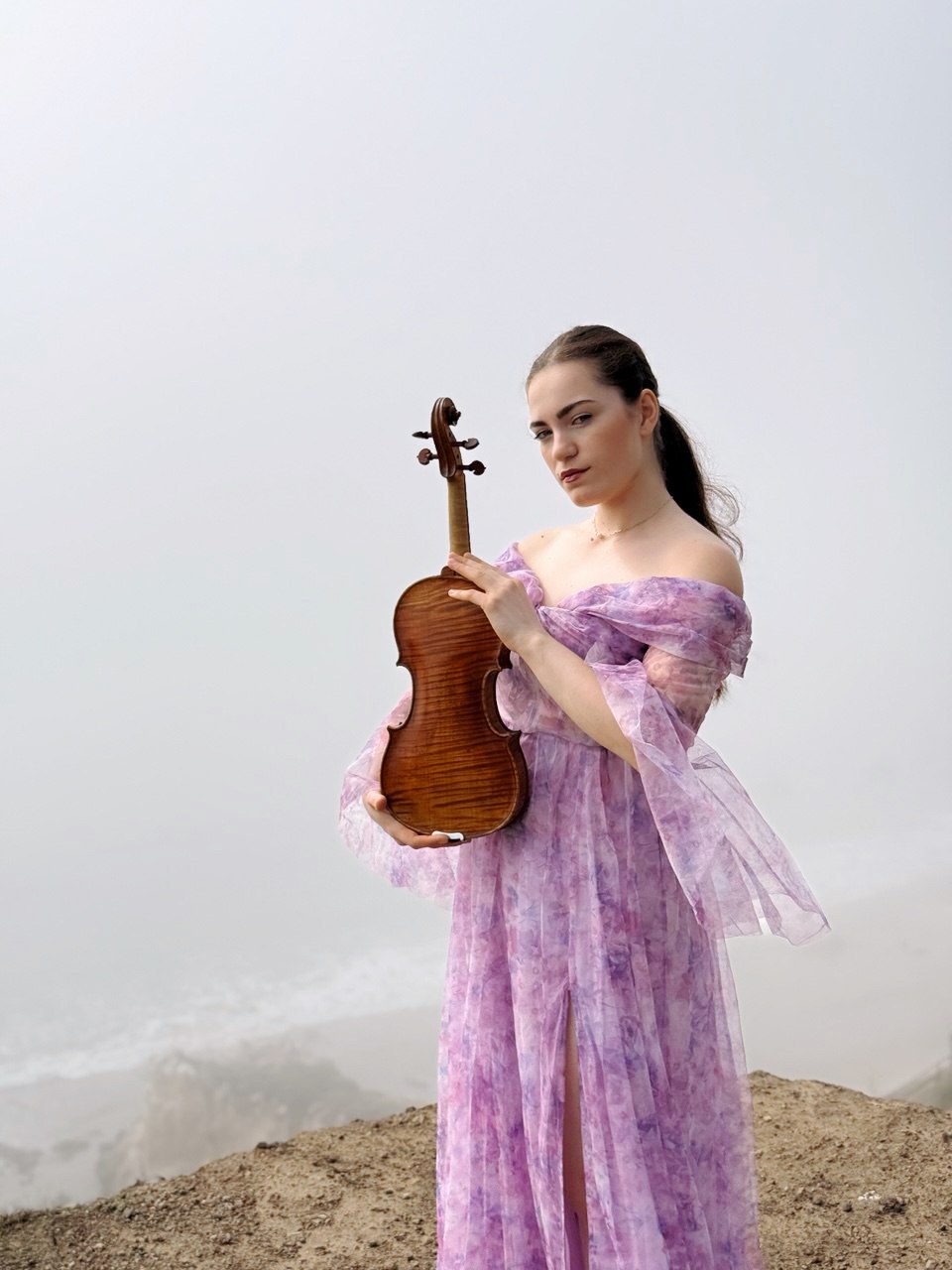 Violinist Sendi Vartanovi in a lilac gown holding her violin outdoors