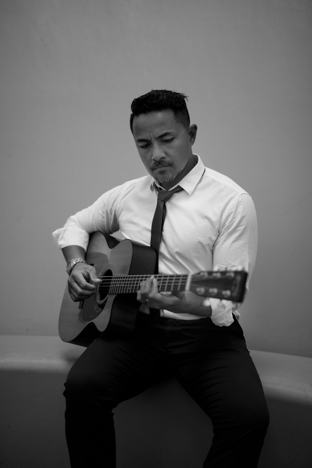 Black-and-white portrait of Steve Amosa playing an acoustic guitar