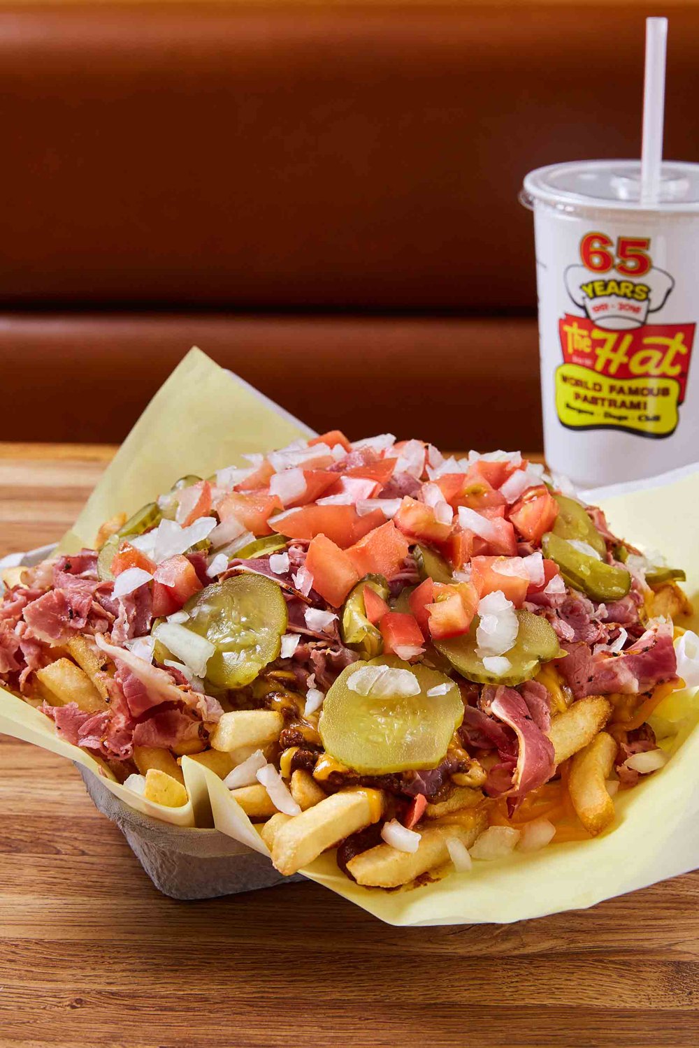 A tray of chili cheese fries topped with pastrami, pickles, tomatoes and onions at The Hat