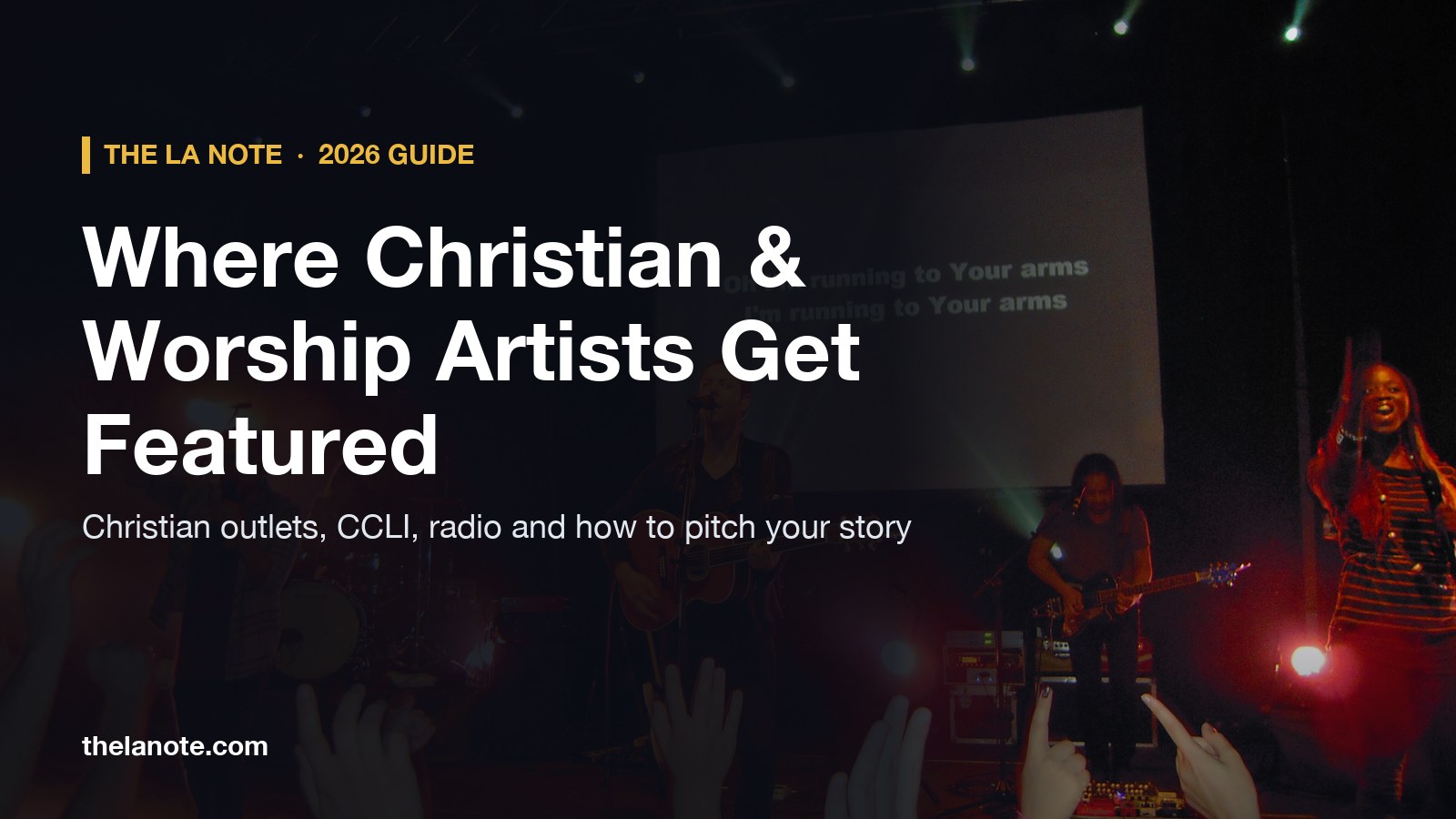 A worship band on stage with lyrics on a screen and hands raised in the crowd